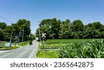 View of An Amish Horse and Carriage Traveling Down a Rural Country Road After Crossing a Rail Road Crossing on a Sunny Spring Day