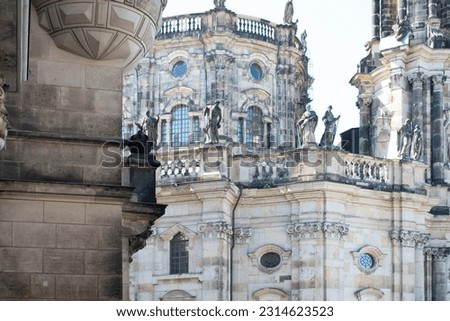 View of an ancient building with grey walls, sculptures, decorative elements and round windows. Grey dirty brick wall in the foreground. Old 
 historical architecture. Dresden, Germany, May 2023