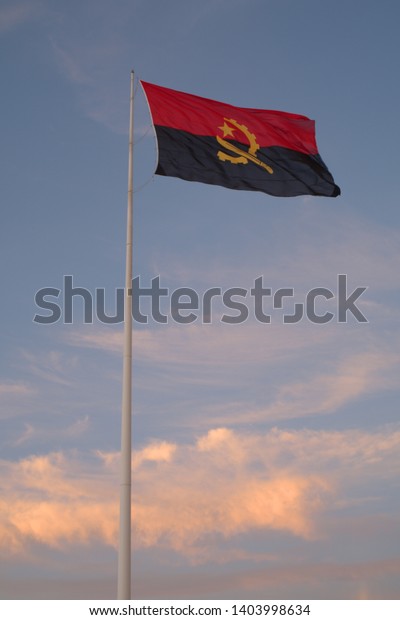 View of Angolan flag on flag pole against blue\
sky, Luanda