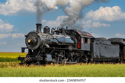 A View of an Antique Steam Passenger Train Approaching, Traveling Thru Rural Countryside, Blowing Smoke, on a Sunny Spring Day - Powered by Shutterstock