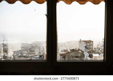 View from an apartment window frame overlooking the rooftops of Kavala Greece in warm sunset light creating a peaceful city panorama