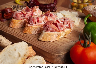 View of a appetizer shot on a rustic wooden table, with a composition that contains Spanish tapas of Iberico ham, chorizo, slabs of parmesan cheese, peppercorns, bread, peppers, olives and tomato - Powered by Shutterstock