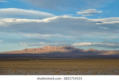 view of a arid desolate landscape with mountains seen in the distance and fluffy clouds in the sky