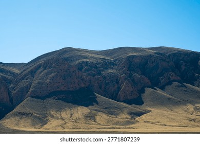 View of an arid rugged mountain range in Middle Atlas Mountains, Morocco featuring steep rocky cliffs and deep shadows across dry slopes under a clear bright blue sky