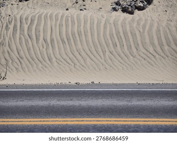 View of an asphalt road in the process of being buried by sand dunes moved by the wind