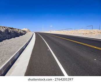 View of an asphalt road with triangular-shaped concrete ditches in an arid desert