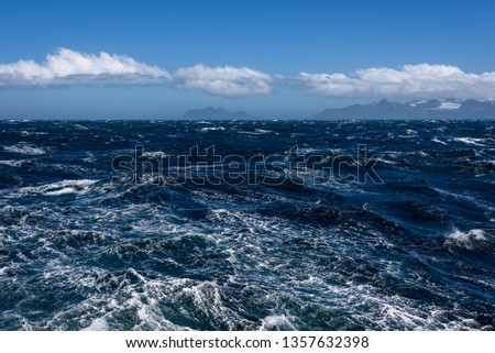 View of Atlantic Ocean and distant mountains, choppy water, calm blue sky with white clouds
