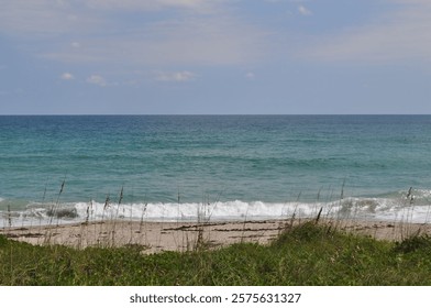 A view of the Atlantic ocean with sandy, grass covered dunes in the foreground. 