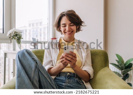 View of attractive woman using her phone .Brunette carre caucasian woman smiling and looking at phone sitting on the chair in room. Concept use technology [[stock_photo]] © 