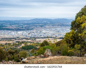 View From An Australian Bush Clearing At A Vantage Lookout Point, Featuring Distant Rolling Hills And Patchy Woodlands. Urban Development At Mid-ground Complete. Dramatic Clouds.