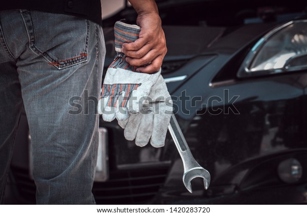 The view\
from the back of the car mechanic is holding the gloves and wrench\
to repair the black car in front of the house. A new service that\
can call a technician to repair at\
home.