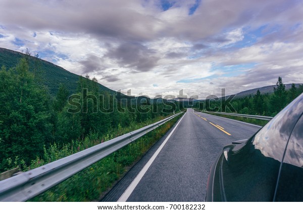 View from\
the back of the driving black car on the background of mountains\
and forest in the Norway. By\
Letowa.
