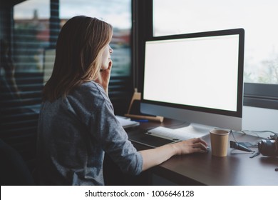 View From Back To Female Student Is Talking On Smartphone Sitting At Desk In Front Of Monitor With Blank Space For Design. Mockup Screen With Copy Space. Woman Makes A Business Call