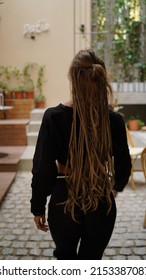 View from the back of a girl with dreadlocks walks around the city. Stylish boho dreadlocks hairstyle. Hippie girl runs down the street. Travel, old town