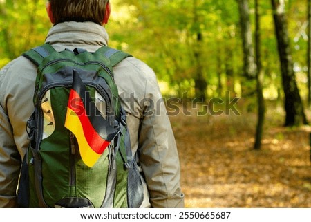 View from the back of a man with a backpack and a German flag, he is a tourist traveler walking through the forest.