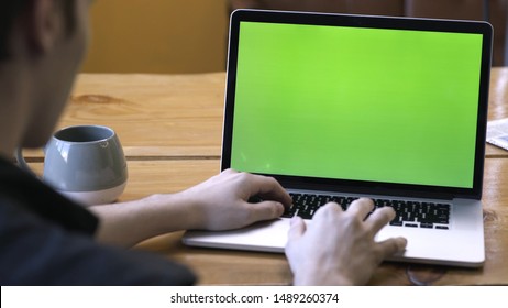 View from the back of man in black shirt sitting at the table and typing on laptop with green chroma key screen. Stock footage. Laptop new technology concept, chroma key green screen - Powered by Shutterstock