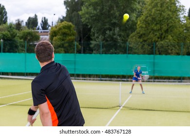 View From The Back On A Male Tennis Player Wearing A Sportswear Serving During The Match On A Court Outdoor In Summer