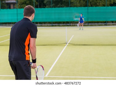 View from the back on a male tennis player wearing a sportswear playing tennis on a court outdoor in summer