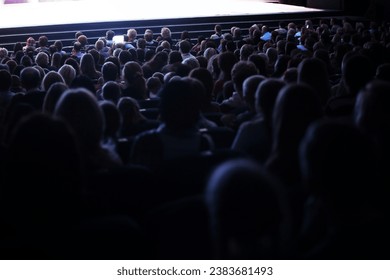 View from the back of a packed auditorium or theatre with people seated in an audience watching a live performance on a stage - Shutterstock ID 2383681493