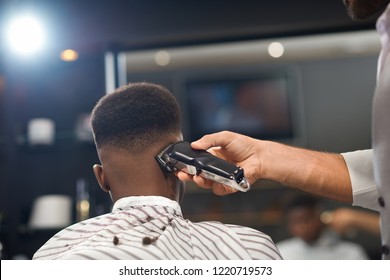 View from back of process of trimming hair of male client in barber shop. Barber keeping clipper in hand and shaving hair to man sitting on chair. Concept of stylish hairdressing and shaving. - Powered by Shutterstock