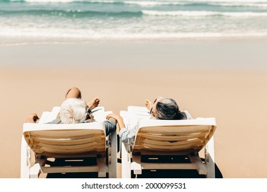 view from the back of a retired couple resting on a adirondack chair by the beach in the sunlight and clean sandy beach. Retirement Planning Ideas and Happy Life.