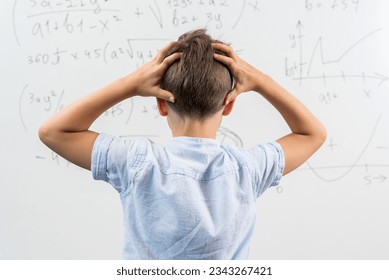 View from the back of schoolboy standing in class against blackboard. Boy holding hands on head. Portrait of shocked and emotional little kid. Back to school. Failing to solve a mathematical equation - Powered by Shutterstock