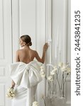 View from the back to the slender young woman in elegant white evening dress with open back. Professional model with white interior.