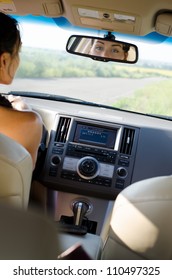 View From The Back Of The Vehicle Of A Woman Driver Looking In Her Rear View Mirror