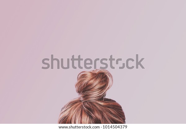 A view of the back of a woman's head. Hair
wrapped in a bun on a light pink pastel background. Content
completion concept.
