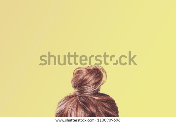 A view of the back of a woman\'s head. Hair\
wrapped in a bun on a light yellow pastel background. Content\
completion concept.