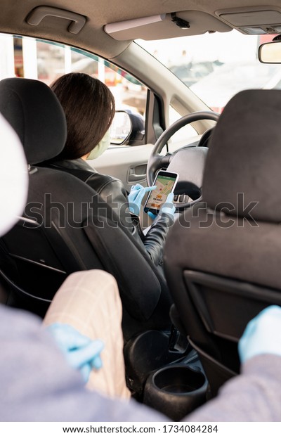 View from backseat of female taxi driver with\
smartphone looking through navigator map while searching for\
address of new client