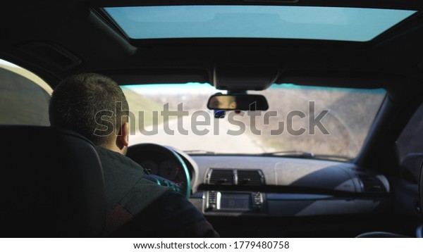 View from\
backseat on young man drives a car on empty road. Guy rides in his\
modern SUV through countryside. Male tourist travels on his auto.\
Concept of journey. Close up Slow\
motion
