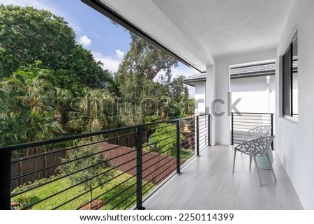 View from balcony of fenced backyard with wooden fences, short grass and tree in the middle, tropical vegetation around, outdoor chairs in gallery, in the Tarpon River neighborhood of the city of Fort