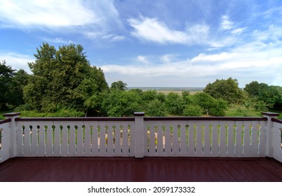 View from the balcony of a wooden house on green trees on a clear summer day. White railings. Red floor.