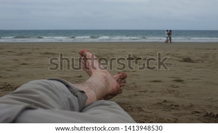View of the bare feet of a man lying on the sand with the sea in the background on a cloudy day