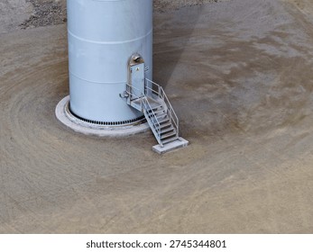 View of the base and foundation of a gigantic wind turbine with a steel ladder at the entrance.