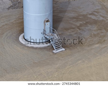 View of the base and foundation of a gigantic wind turbine with a steel ladder at the entrance.