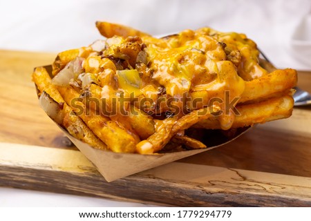 A view of a basket of loaded fries, on a wooden cutting board.