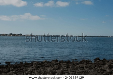 View  of bay on bayside at Jungle Prada de Narvaez Park looking west in St. Petersburg, Florida on a sunny day. Rocks on the shoreline. Blue sky with white clouds and calm water