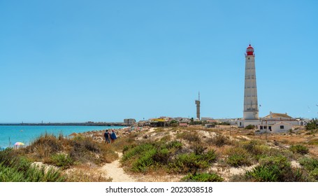 View of the beach of the Portuguese island of Farol with a lighthouse and a couple walking along the path. Ria Formosa