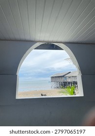 View of a beach through an arch-shaped window with palm trees and shoreline.