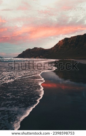 View of beautiful high tide during the golden hour on the Famara.´ Beach in Lanzarote - Canary Islands. Photo of sunset on the beach with reflection of ocean and pink sky and cliff on background.