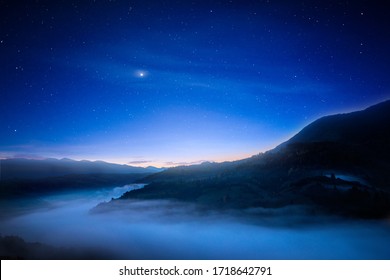 View Of Beautiful Night Sky With Stars In Foggy Mountain Valley. Scenic Landscape Of Misty Hills Under Blue Starry Sky. Concept Of Astrology And Magical Nighttime.