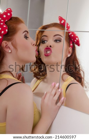 View of a beautiful redhead girl with colorful pinup clothes next to a mirror wall.