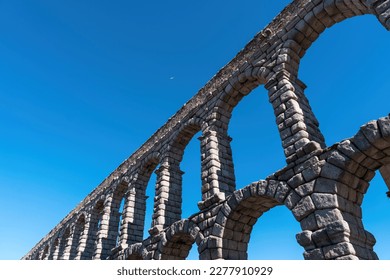 View of beautiful Roman aqueduct of Segovia Spain and tiny plane against a blue sky 