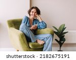 View of beautiful woman in home with phone .Brunette carre hair look and smiling to camera sitting on the green chair at home. Relax, lifestyle concept 