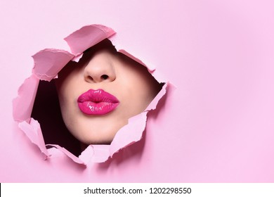 View of beautiful young woman with perfect lips makeup through hole in color paper. Space for text