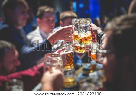 View of beer festival, gold coloured beer glasses assortment in a pub, german unfiltered wheat beer, people cheering up and toasting with glasses of light lager, Oktoberfest view