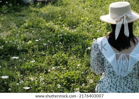 View from behind of a Asian lady sitting in wild flower field in a sunny spring day. 