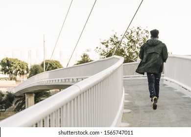 View From Behind Attractive Young Black African Man With Cool Casual Wear Running On A Modern Bridge In The City, Lifestyle Concept